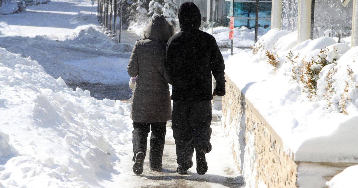 Couple walking along a snow covered sidewalk trying to avoid injury from a slip and fall accident.